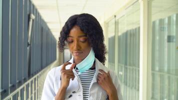 africano americano fêmea médico remove uma médico mascarar dentro moderno clínica. fim do quarentena. Pare vírus video