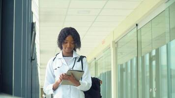 afrikanisch amerikanisch Schüler Praktikant mit ein Tablette im das Krankenhaus. Neu modern völlig funktional medizinisch Einrichtung. Konzept von Medizin, Gesundheit Pflege und Menschen, online Bildung video