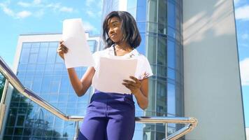 Adult african american young businesswoman works with documents near modern office building. End of quarantine video