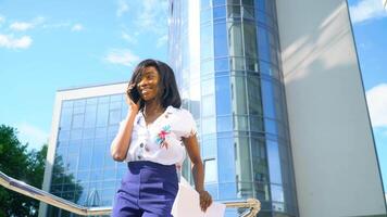 adulto africano americano giovane donna d'affari è parlando su Telefono al di fuori vicino moderno ufficio edificio video