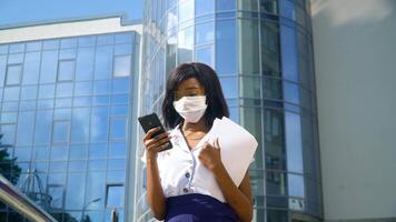 Elegant beautiful african american businesswoman in protection mask using social networks on her smartphone. Having nice appearance and charming smile video