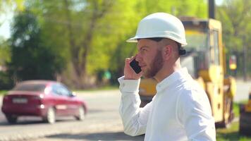 manager van de reparatie werken tegen de achtergrond van een weg bouw plaats pratend Aan de telefoon. weg reparatie concept video