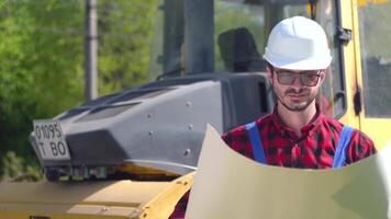 The worker in uniform looks at the drawings on the background of the road under construction video