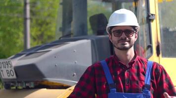 Porträt von ein Baumeister im ein Helm und Uniform gegen das Hintergrund von ein Konstruktion Seite? ˅ auf ein sonnig Sommer- Tag. Straße Reparatur Konzept video