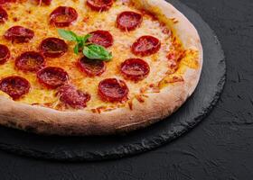 Pepperoni Pizza with Basil and Parmesan Cheese on Black Stone Plate photo