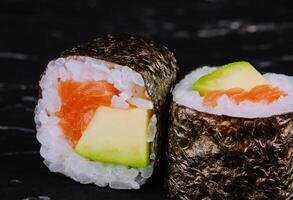 Sushi rollos con salmón y aguacate en un negro Roca foto