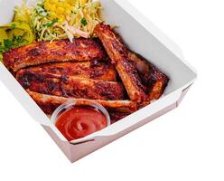 Tasty grilled ribs with vegetables in box photo