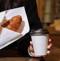 Woman holding a mug of coffee and a croissant in her hands in coffee shop photo