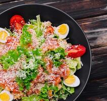 Salad with salmon, lettuce, boiled eggs, cherry tomatoes and parmesan cheese photo