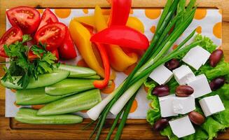 onions, cucumbers, peppers, tomatoes and feta cheese with olives on a wooden tray photo