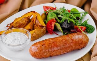 Roasted sausages with baked potatoes and green salad and chicken with cheese photo