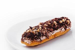 eclair with chocolate and nuts on a white plate photo