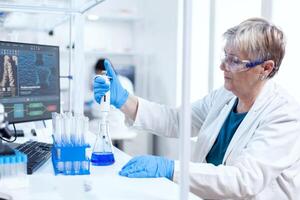 Senior genetic researcher taking sample from glass flask using molecular dispenser. People in innovative pharmaceutical laboratory with modern medical equipment for genetics research. photo