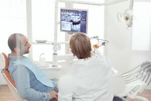 dentista médico y paciente mirando a digital diente radiografía en estomatología hospital oficina. enfermo paciente sentado en dental silla preparando para odontología cirugía durante somatología cita foto