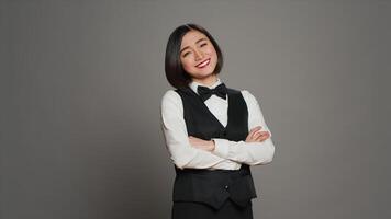 Asian receptionist posing with arms crossed on camera, feeling confident and professional in a formal suit and tie. Woman with front desk staff occupation, greeting guests in studio. Camera A. photo