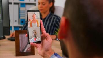 Entrepreneur talking on videocall with company manager and executive administrator sitting on desk in corporate building office using smartphone. Financial businessman using modern technology. photo