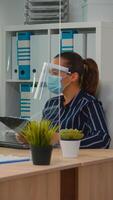 Immobilized freelancer with protection mask in wheelchair having videomeeting during a coronavirus pandemic in new normal business office. Freelancer working in company respecting social distance. photo