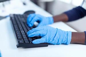 Close up of african researcher holding hands on computer keyboard Black healthcare scientist in biochemistry laboratory wearing sterile equipment. photo