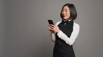 Restaurant hostess texting messages to confirm reservations on phone app, working in catering and serving industry. Asian waitress using smartphone online websites, social media. Camera A. photo