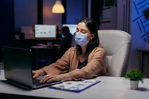 mujer de negocios trabajando difícil a terminar un fecha límite debido a covid19 brote. mujer siguiendo social distanciamiento reglas debido a coroanvirus pandemia mientras trabajando tarde horas a el oficina. foto