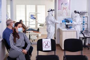 Stomatology dentist dressed in ppe suit taking patient x-ray from receptionist in clinic hallway, keeping social distancing during global pandemic with coronavirus. photo