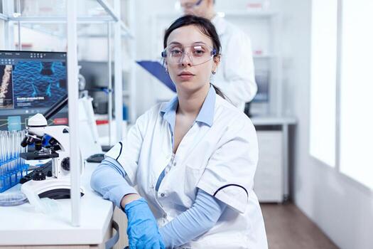 Portrait of successful scientist in microbiology laboratory wearing protection equipment. Chemist wearing lab coat using modern technology during scientific experiment in sterile environment. photo