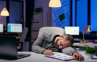 cansado empresario dormido en su lugar de trabajo en escritorio. trabajador obsesivo empleado que cae dormido porque de mientras trabajando tarde a noche solo en el oficina para importante empresa proyecto. foto