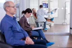Senior woman sitting on chair in dental office listening dentist talking about diagnosis for teeth cavity looking at digital x-ray radiography. Patients filling form in waiting area. photo