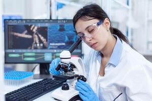 hembra científico en moderno laboratorio usos microscopio para medicina vacuna. médico técnico vistiendo blanco Saco en estéril laboratorio haciendo solución análisis. foto