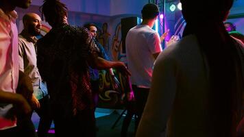 Diverse people partying at nightclub, enjoying disco party on dance floor with cool DJ music. Smiling men and women having fun together at discotheque, celebration event. Handheld shot. photo