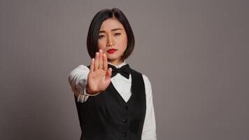 Asian administrator showing stop sign with palm raised in studio, presenting negative symbol and expressing disapproval. Woman receptionist doing no gesture, being displeased. Camera B. photo