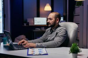 Concentrated young businessman working in office alone at night. Smart businessman sitting at his workplace in the course of late night hours doing his job. photo