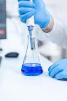 Scientist holding dispenser on test tubes in clinic pharmacy and medical research laboratory. Senior professional chemist using pippete with blue solution for microbiology tests. photo