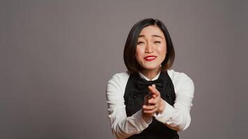 Restaurant hostess clapping hands and celebrating for someone, cheering and saying congratulations in studio. Asian waitress with uniform and apron applauding a person, acclaim. Camera B. photo