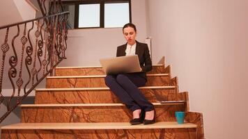 Employee using laptop overworking on deadline sitting on stairs in finance corporate company. Executive manager doing overtime at job on staircase businesspeople working in modern financial building. photo