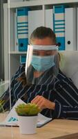 Businesswoman with visor and protection mask working in new normal business office. Freelancer discussing with colleague in financial company respecting social distance during global pandemic. photo