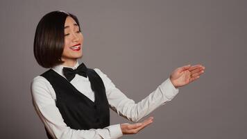 Reception staff doing web advertisement over grey background, pointing at something aside for a marketing commercial. Asian employee working on a promotional ad in studio. Camera B. photo