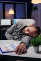 Manager napping on desk because of overwork in workplace. Workaholic employee falling asleep because of while working late at night alone in the office for important company project. photo