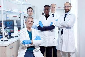 Team of professional scientists standing together in research lab looking at camera posing with arms crossed. African healthcare scientist in biochemistry laboratory wearing sterile equipment. photo