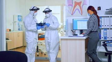 Orthodontics doctors with face shield and ppe suit discussing in reception about teeth x-ray while patient waiting during global pandemic. Concept of new normal dentist visit in coronavirus outbreak. photo