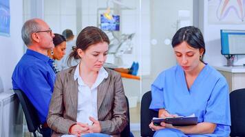 Nurse taking notes on clipboard about patient dental problems waiting for orthodontist sitting on chair in waiting room of stomatological clinic. Assistant explaining medical procedure to woman. photo