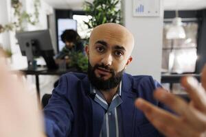 Executive manager looking at camera while presenting project during video call on smartphone. Arab startup entrepreneur holding mobile phone and explaining strategy in online meeting photo