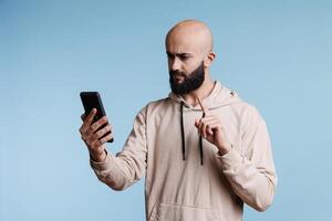 Serious arab man talking in smartphone videoconference and showing one with index finger. Person pointing while having remote communication using mobile phone videocall app photo