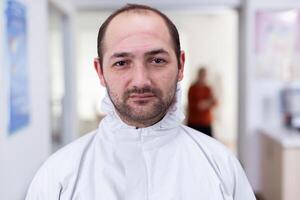 retrato de agotado médico mirando en cámara vistiendo ppe traje sin cara proteger sentado en silla en esperando habitación clínica. concepto de nuevo normal en coronavirus brote. foto