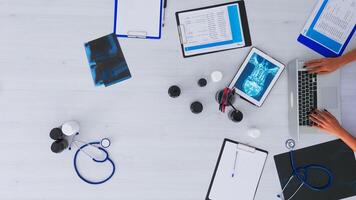 Top view of woman doctor hands typing on laptop sitting on desk with x-ray and medical equipment all around. Assistant working in health clinic using modern devices. Copy space, flat lay concept photo