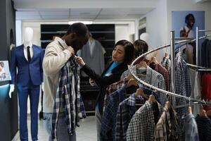 Boutique conslutant providing assistance in choosing casual clothes while customer trying on apparel. Shopping mall showroom worker offering help in selecting casual shirt photo