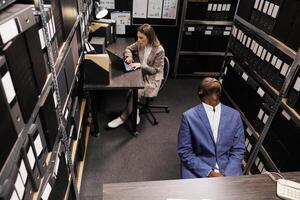 Top view of private detective having pensive expression, brainstorming ideas to solve crime case in arhive room. Diverse investigators working overtime at investigation, analyzing new evidence photo