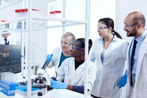Group of multiethnic pharmacy scientists in lab coats working together in modern facility. Black healthcare researcher in biochemistry laboratory wearing sterile equipment. photo