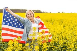 attractive woman holding an American flag in the wind in a field of rapeseed. Summer landscape against the blue sky. Horizontal orientation. photo