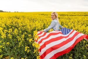 attractive woman holding an American flag in the wind in a field of rapeseed. Summer landscape against the blue sky. Horizontal orientation. photo